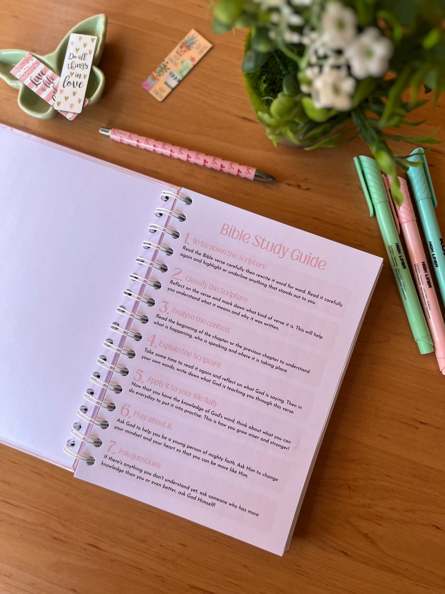 Open Bible Study Guide on a wooden table with markers and flowers