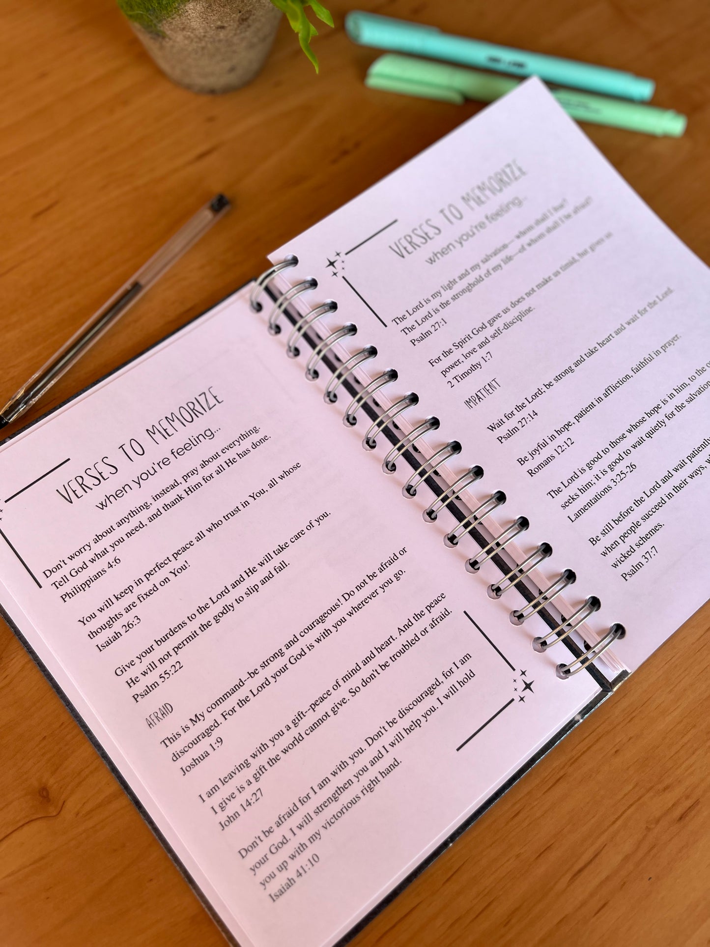 Open notebook with spiral binding on a wooden surface, featuring Bible verses.