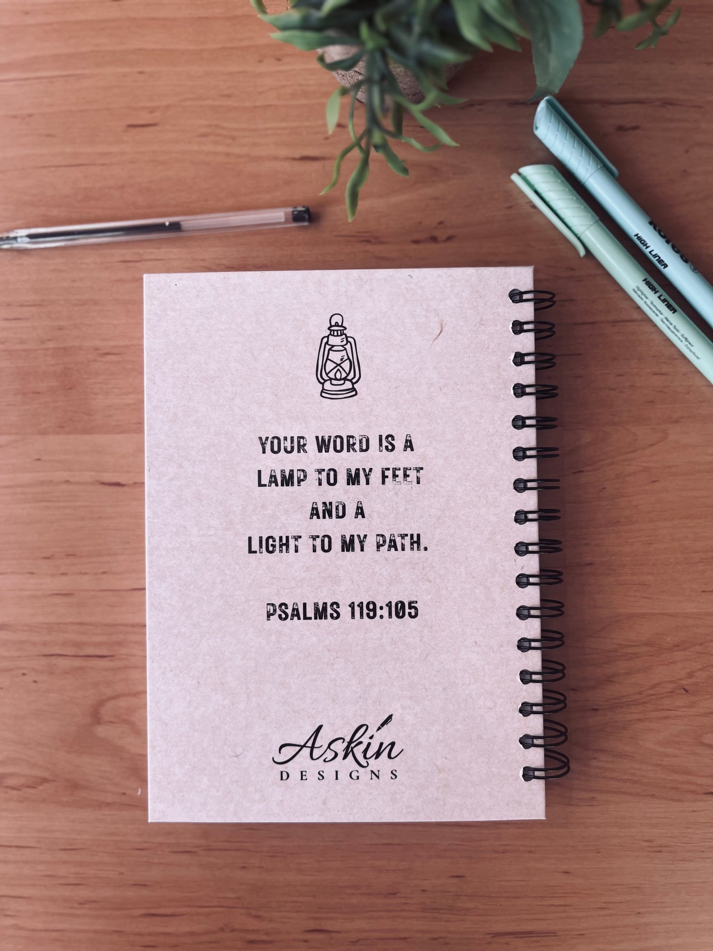 Notebook with Bible verse and branding on a wooden surface