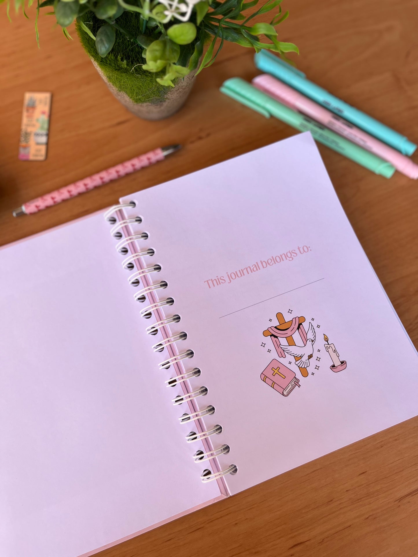 Spiral-bound notebook with decorative cover on a wooden surface with stationery items.