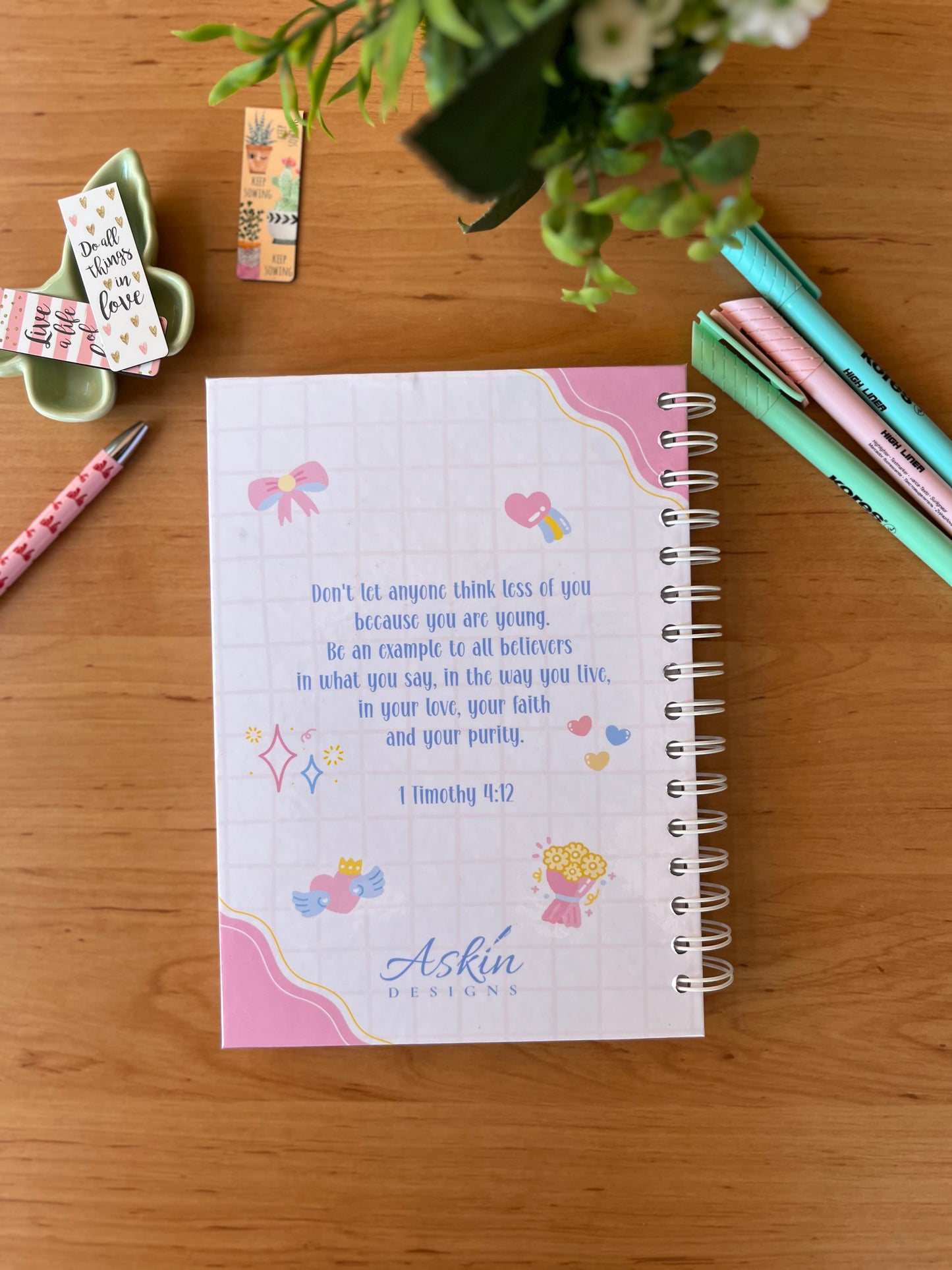 Notebook with Bible verse on a wooden surface with stationery items.