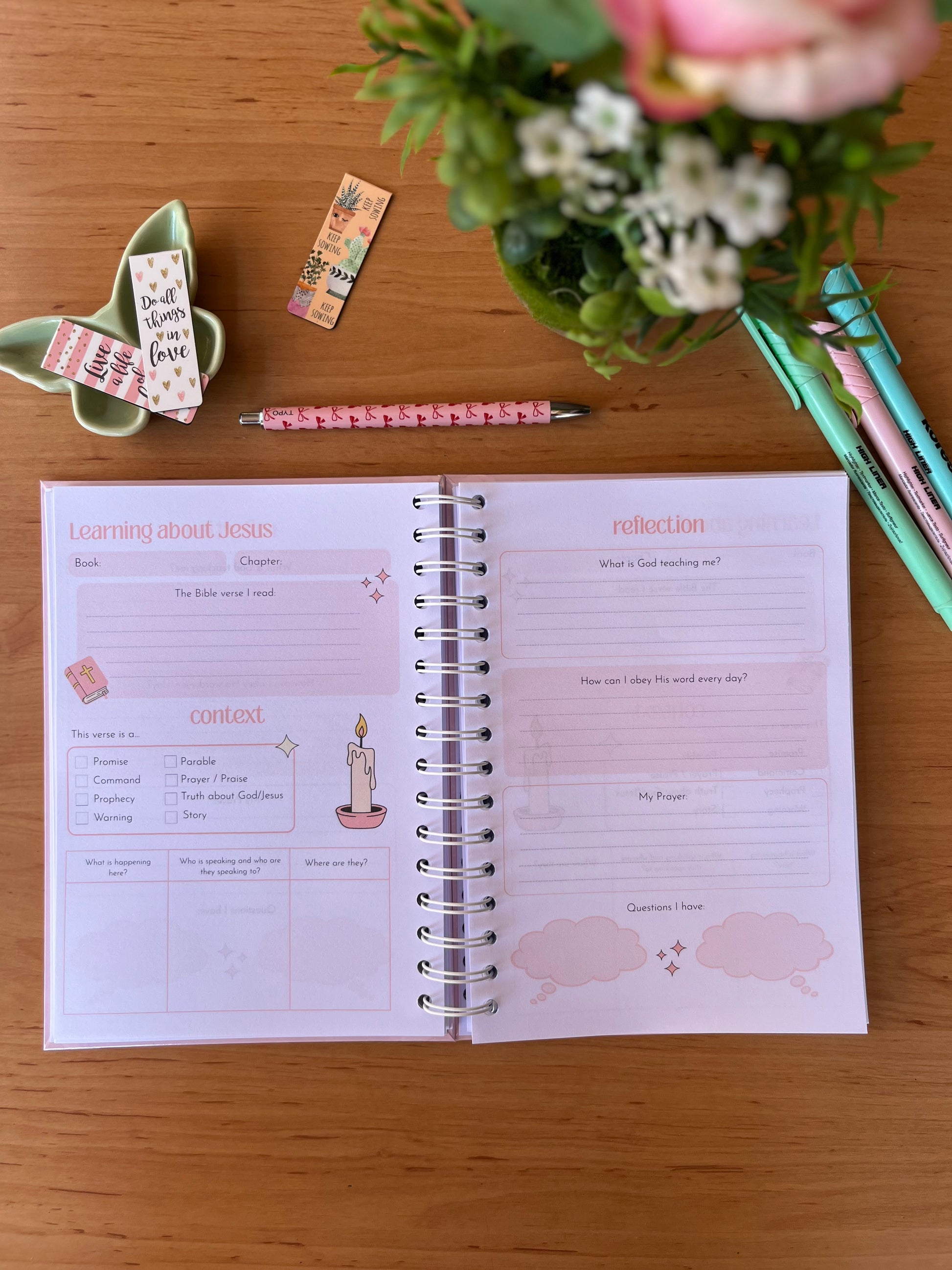 Open spiral-bound Bible Study Journal on a wooden surface with stationery items.