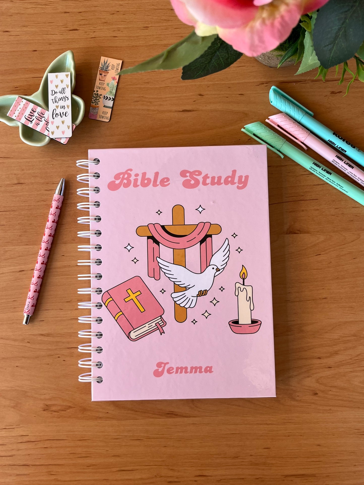 Pink notebook with Bible Study design on a wooden surface with stationery items.